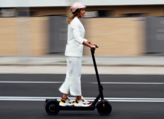 Jazdec s prilbou ide na elektrokolobežke po cyklotrase v meste, dodržiava pravidlá a jazdí bezpečne medzi chodcami a cyklistami.